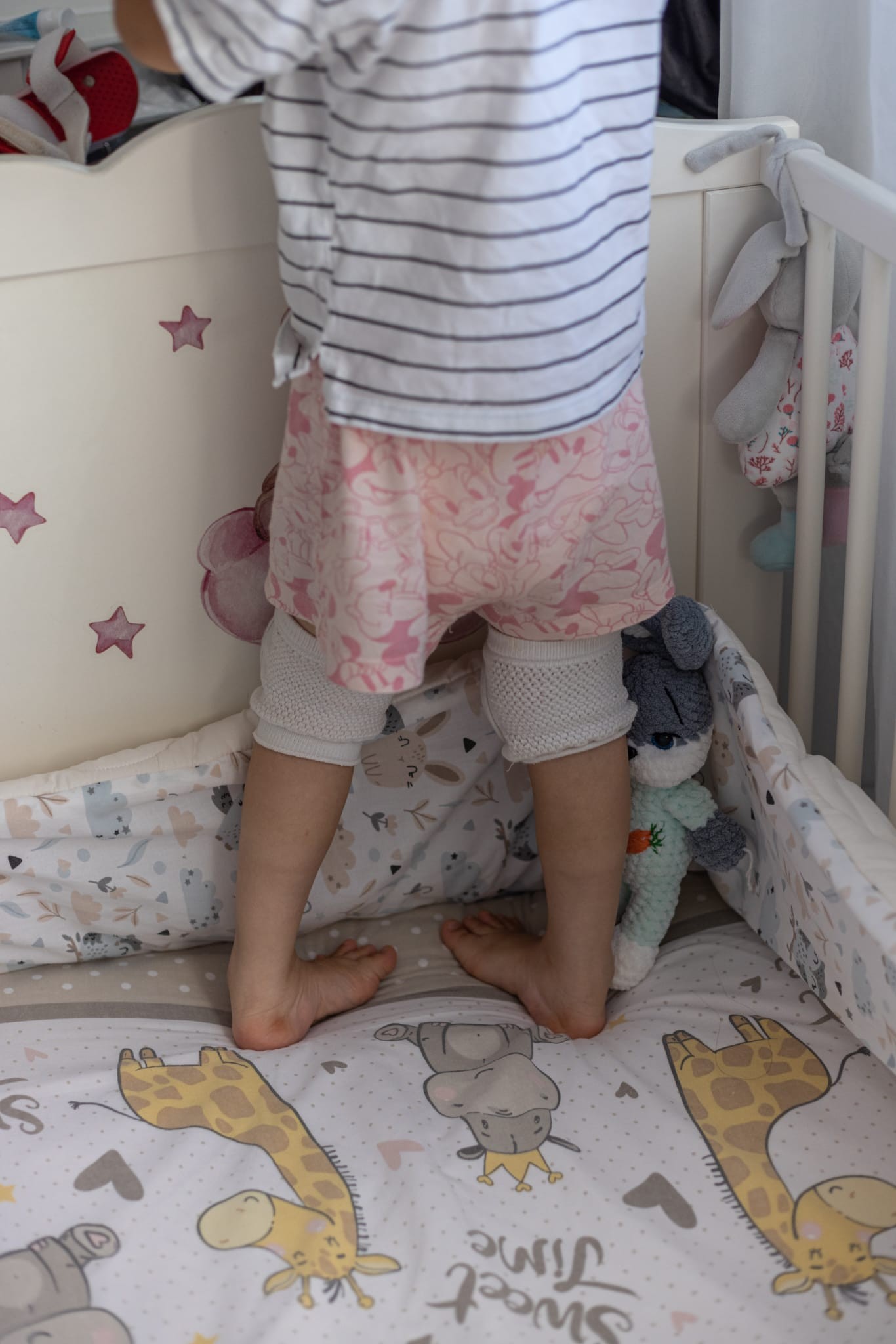 Copil mic în picioare în pătuțul de lemn, cu genunchiere de protecție